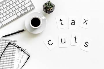 Tax cuts copy on accountant work place with keyboard, coffee and glass on white desk background top view