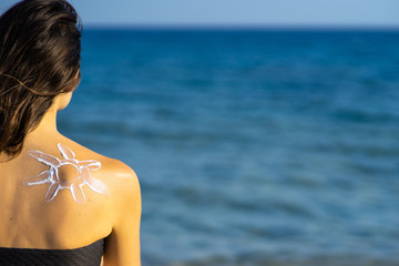 skin protection - young woman with sun cream on her back at the sea