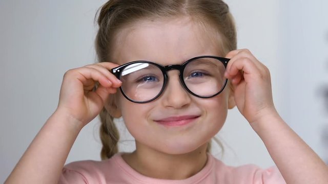Small kid squinting eyes putting on eyeglasses and smiling, farsightedness