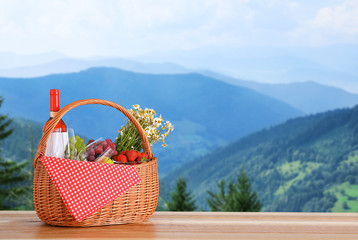 Picnic basket with wine and products on wooden table outdoors, space for text