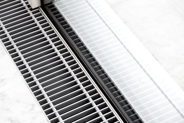 Heating grille with floor ventilation in white stone flooring near the panoramic window, close up...