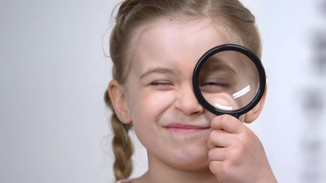 Curios female kid looking through magnifying glass, eyesight examination, health