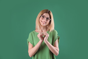 Portrait of woman making heart with her hands on color background