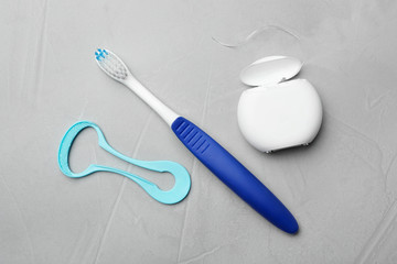Tongue cleaner, dental floss and toothbrush on grey background, flat lay