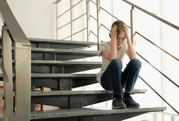 Sad little boy sitting on stairs indoors