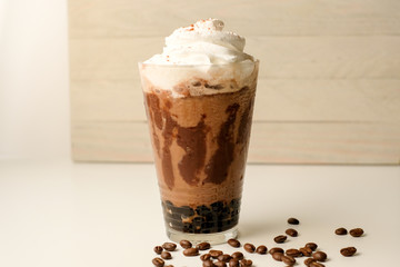 Ice coffee in the glass topped whipping cream with coffee beans. Cold summer drink on wooden background and copy space. Advertising for caramel mocha and chocolate beverage for the cafe.