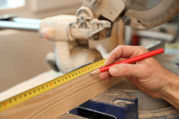 Working man measuring timber strip in carpentry shop, closeup