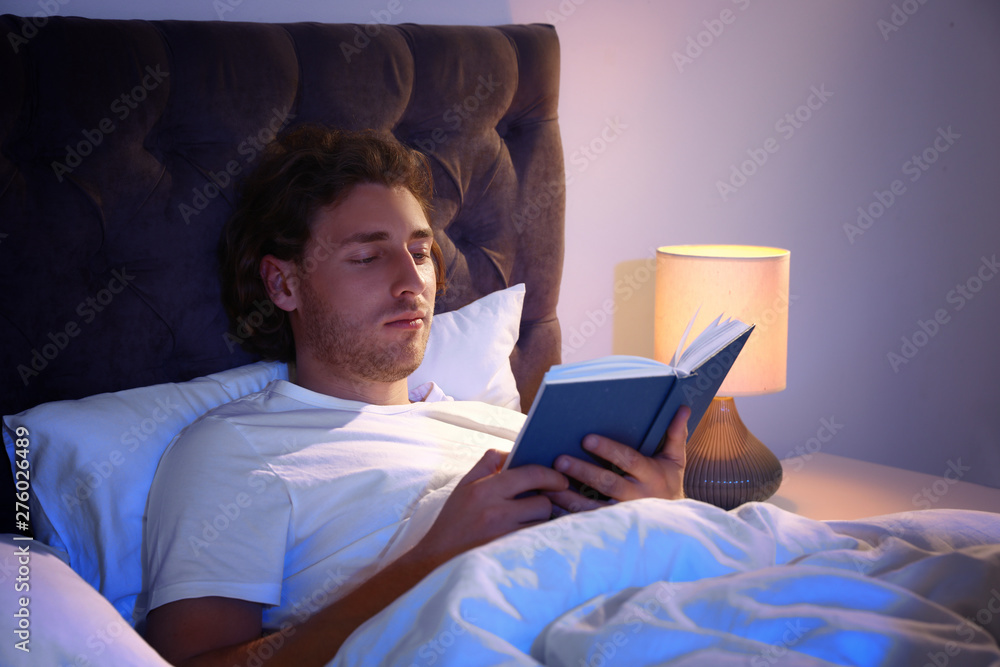 Poster handsome young man reading book in dark room at night. bedtime