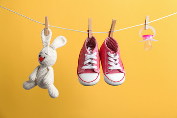 Small shoes, toy bunny and pacifier hanging on washing line against color background. Baby...