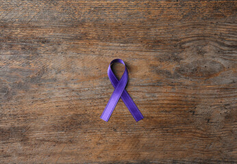 Purple ribbon on brown wooden background, top view. Domestic violence awareness