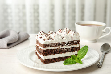 Tiramisu cake with cup on table against light background