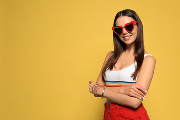 Portrait of beautiful young woman with heart shaped sunglasses on color background. Space for text