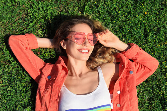 Portrait of happy woman with heart shaped glasses on green lawn, top view