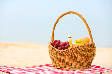 Fototapeta na wymiar Wicker basket with food and juice on blanket near sea, space for text. Summer picnic