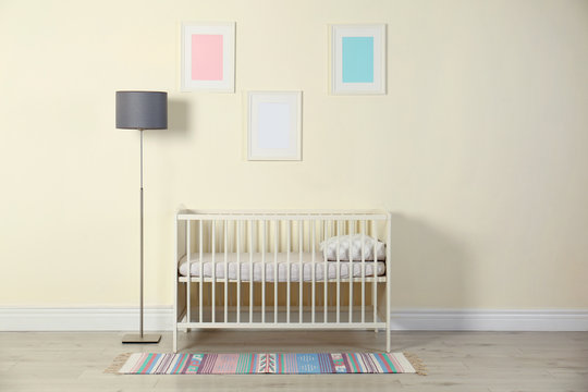 Crib and floor lamp near light wall in baby room interior