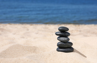 Fototapeta na wymiar Stack of stones on sand near sea, space for text. Zen concept