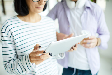 Close-up of content mobile woman in stripped sweater discussing ideas with colleague while checking connection on tablet