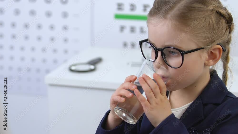 Wall mural small girl in eyeglasses taking pill with water at medical exam, treatment