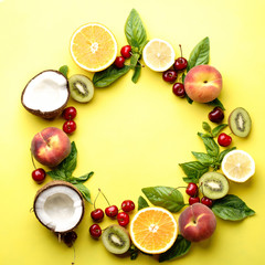 Summer vitamin food concept, various fruit and berries. Peach, kiwi, lemon, cherries, oranges and coconut, creative flat lay on yellow background, top view copy space