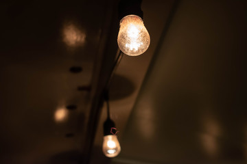 Two large lightbulbs in a string of lights hang on the ceiling of a house's patio at night.