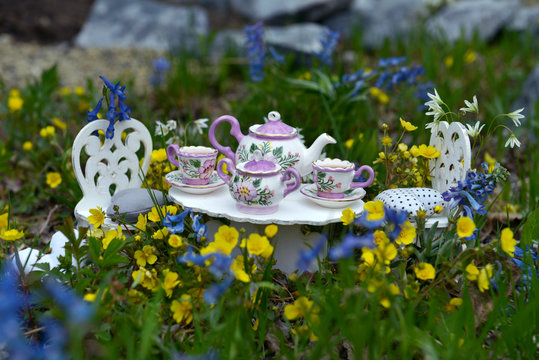 Tiny table with small dishware and tea cups, small chairs in spring flowers.