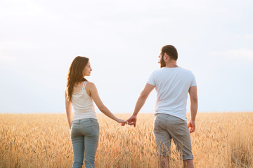 Young married couple holding hands in the sunset field background. Woman and man in love holding hearts. Human relationships and romance