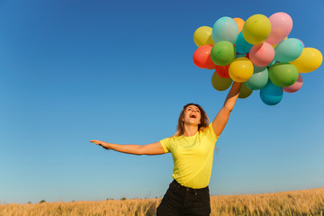 Young girl jumping high in blue sky with bunch of multicolored balloons