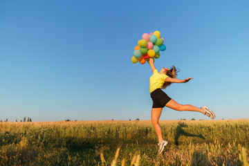 Happiness, dream, inspiration, motivation, summertime. Happy young carefree woman jumping with multicolored balloons at sunset