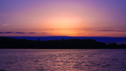 Very romantic sunrise over the water. Silhouette of an island in the distance with vegetation. Idyllic landscape with soft lights and colors in the sky.