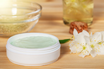 Obraz na płótnie Canvas Jar of cream made from natural plant ingredients, oils and herbs, jasmine flowers on a light wooden background - preparation of organic cosmetics concept, close up