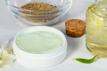 Jar of cream made from natural plant ingredients, oils and herbs, jasmine flowers on a white wooden background - preparation of organic cosmetics concept, close up