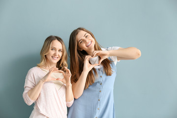 Portrait of happy mother and daughter making hearts with their hands on color background