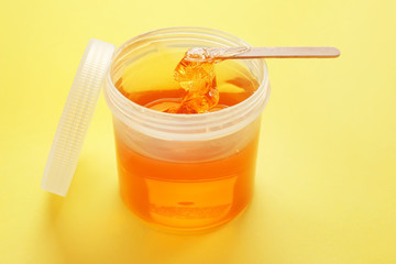 Container with sugaring paste for hair removal on color background