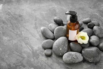 Obraz na płótnie Canvas Bottle of shampoo, flower and spa stones on grey background