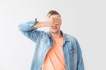 Young man covering his eyes on grey background