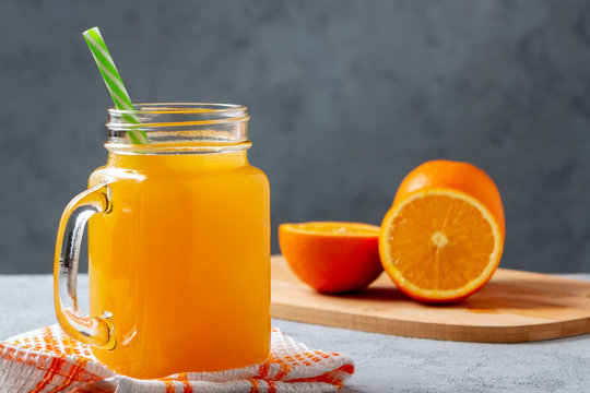 Freshly made citrus juice from oranges in a jar-mug with a straw on gray table