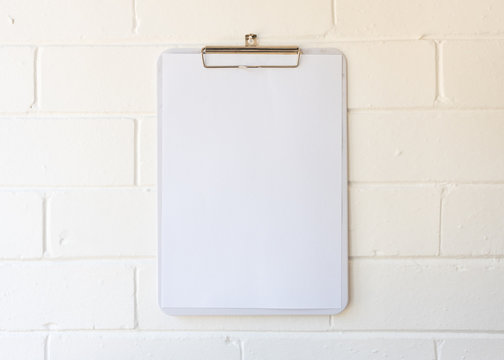 Close up of blank A4 page on clipboard hanging against white painted brick wall