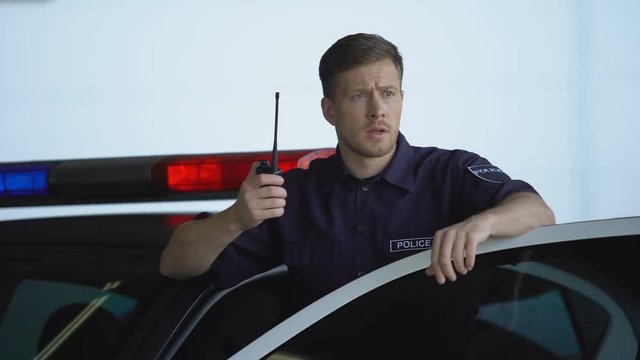 Worried policeman calling for help on two-way radio in patrol car, offence, law