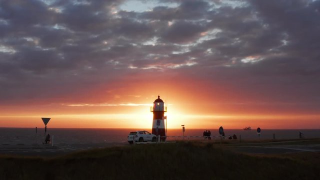 The lighthouse of Westkapelle during a bright orange sunset, with a lot of wind. Aerial shot.