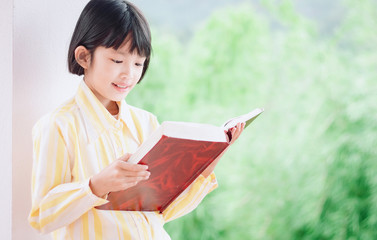 Fototapeta premium Cute little girl reading book green nature background