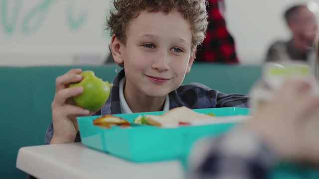 Portrait Of Cute Boy Eating An Apple During Lunch At School. Happy Kids Having A Lunch Time In A School Cafeteria.