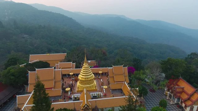 A birds eye view shot of a golden stupa in the middle of a palatial building surrounded by trees at the top of a mountain 