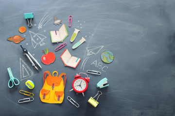 education and back to school concept. shapes cut from paper and painted of backpack, books, chemistry flask and apple over classroom blackboard with funny sketches. top view, banner