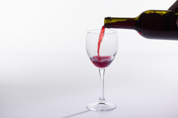 Red wine pouring into glass from bottle on white background with copy space