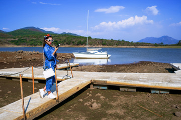 La joven está parada con su celular en el embarcadero del lago.