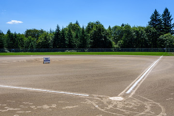 Freshly groomed baseball field with Field Reserved sign, empty baseball field on a sunny day with woods and blue sky in the background