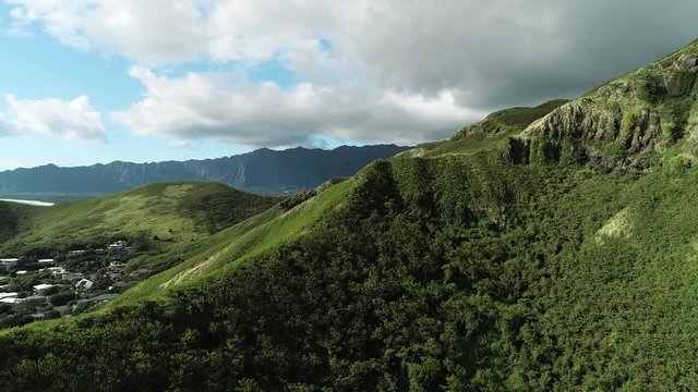 Aerial view of Lanikai beach, Honolulu, Hawaii, low angle view with drone camera moving forward, green mountain ridge with clouds in the background, camera revealing small town, color graded