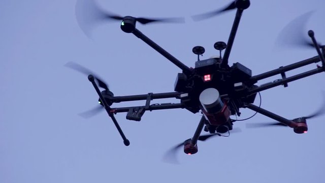 Close-up of quadcopter flying in sky. Clip. Large quadcopter with powerful motors flying on background blue sky. Quadcopter with six motors for long air