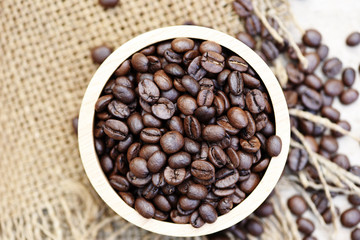 Roasted coffee beans in a wooden bowl on sack background