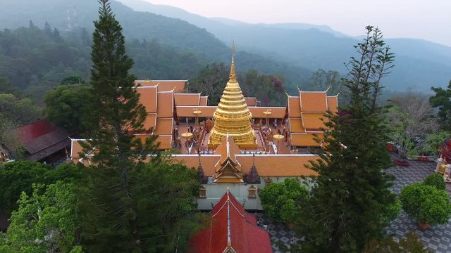A birds eye view shot of a golden stupa in the middle of a palatial building surrounded by trees at the top of a mountain 